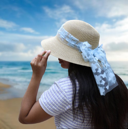 Beige straw round hat with blue ribbon worn by woman on beach with ocean background