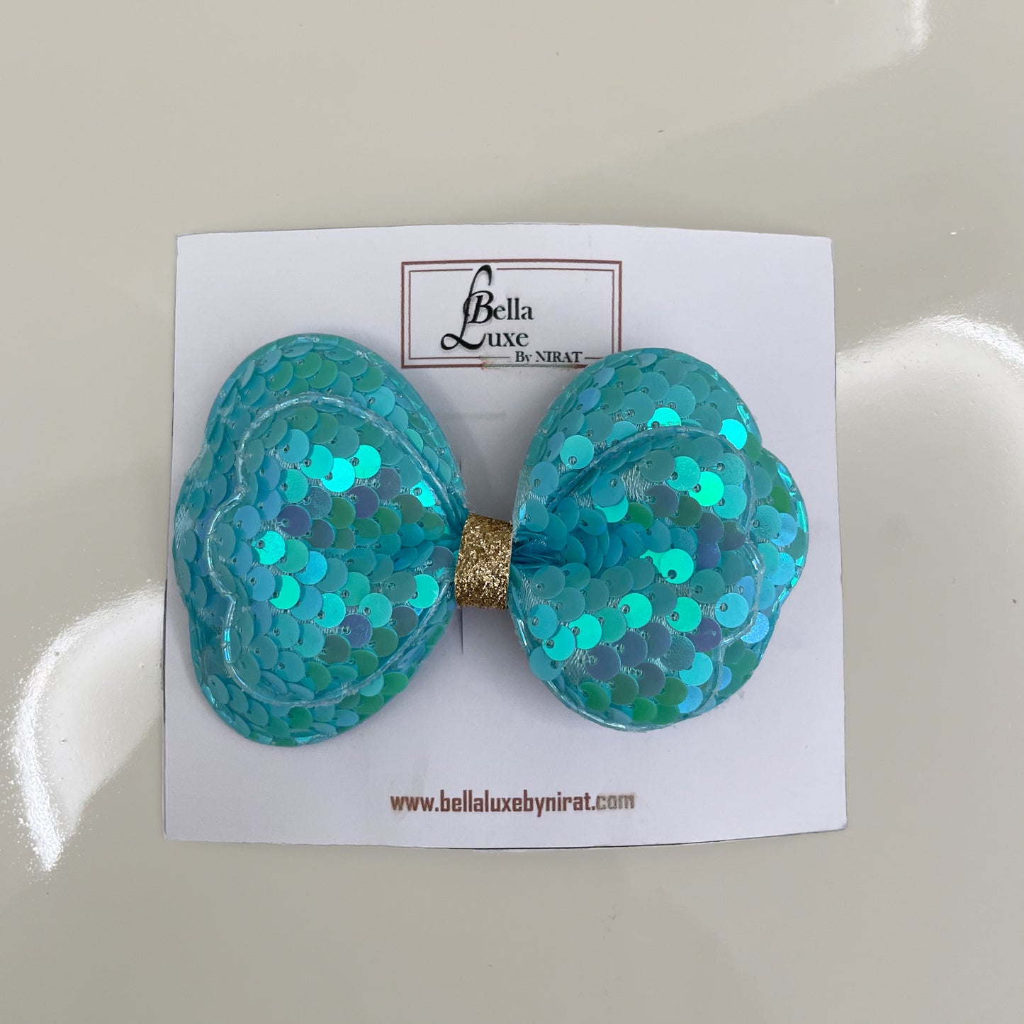 Vibrant Sequined Bow Clips in turquoise blue with gold center on white Bella Luxe card