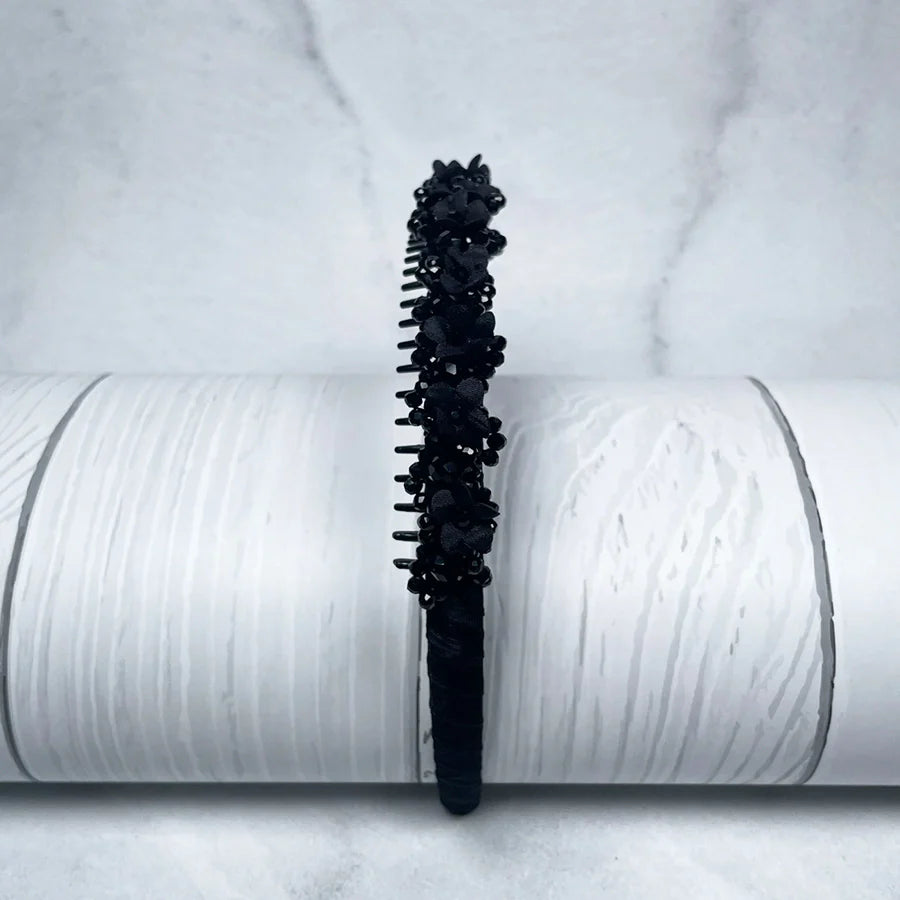 Black embellished headbands for women decorated with beads and floral accents on white textured background