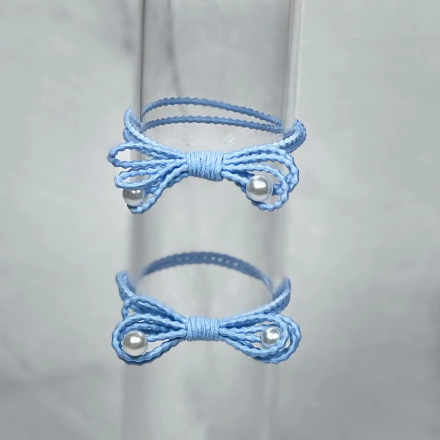 Light blue bow hair ties for women with pearl accents on a clear display stand