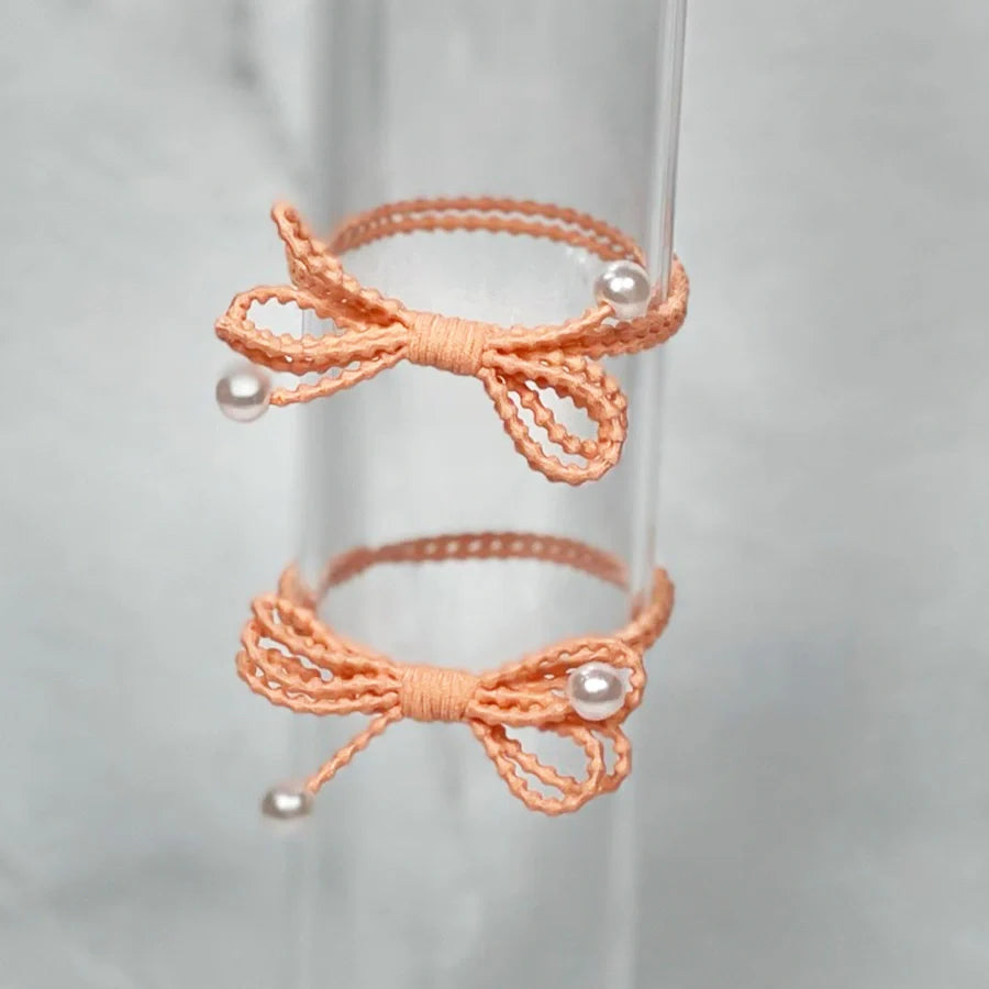 Peach-colored bow hair ties for women with pearl accents on translucent display stand