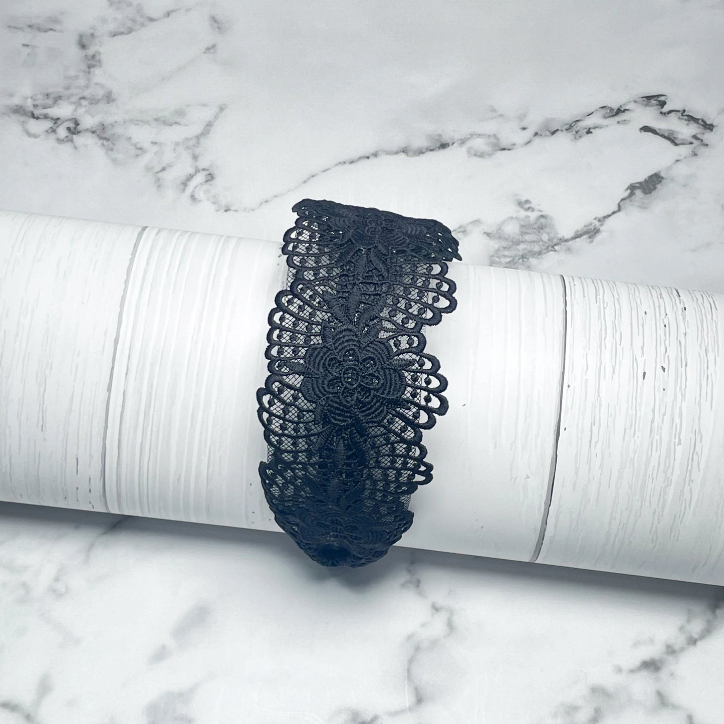 Black broad lace hairbands with floral pattern displayed on white textured surface
