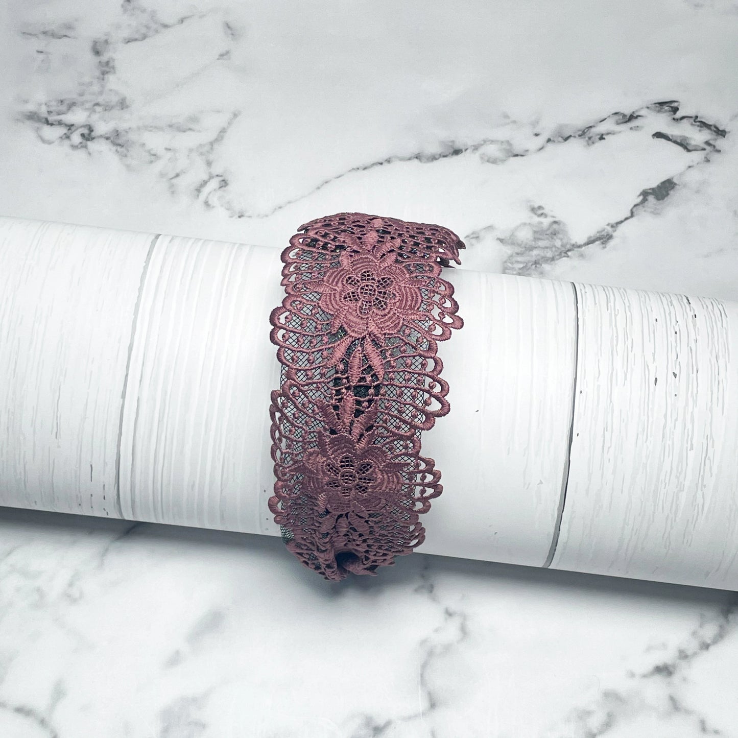Purple broad lace hairbands with floral patterns displayed on a white cylindrical stand