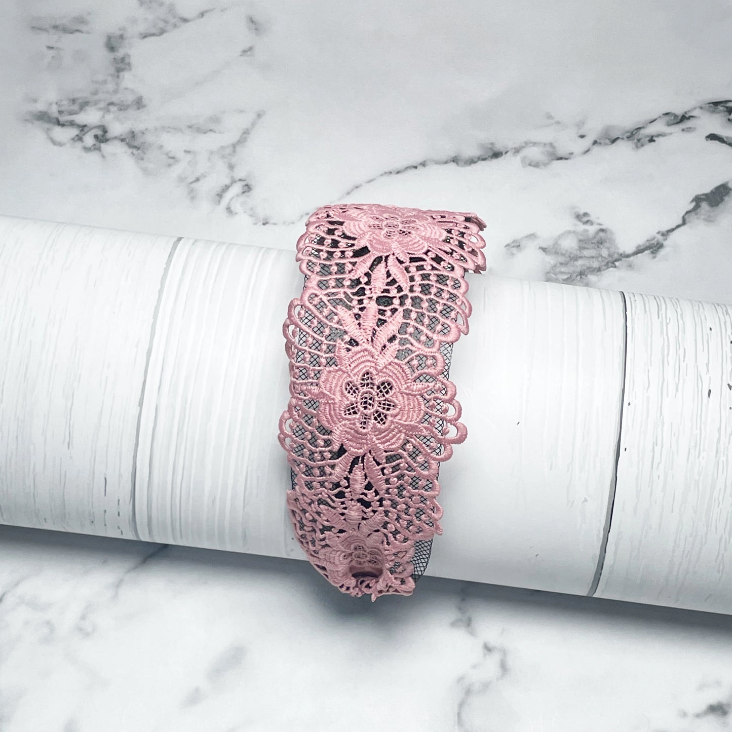 Pink broad lace hairbands with floral pattern displayed on white marble background