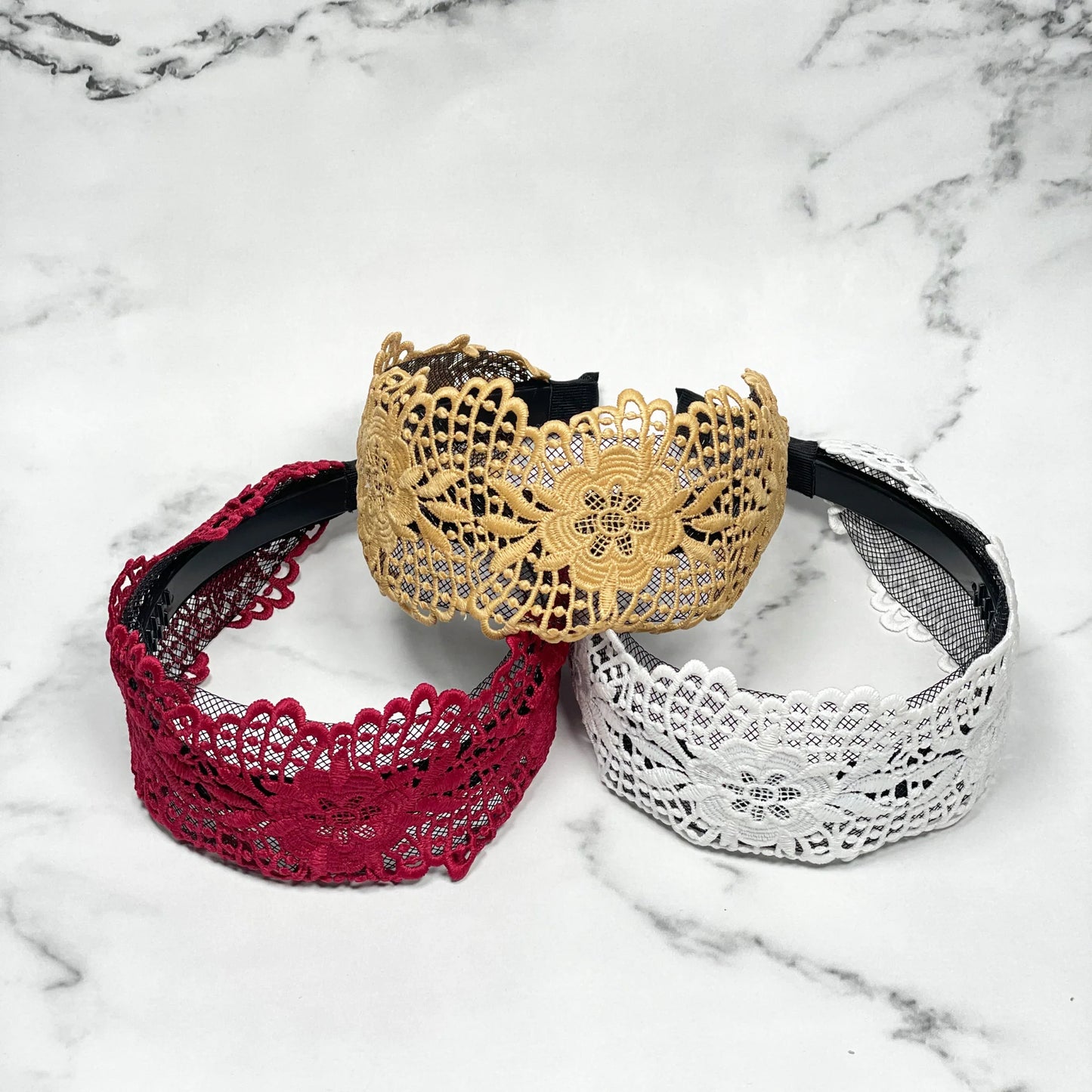Set of broad lace hairbands in red white and beige with floral patterns on a marble surface