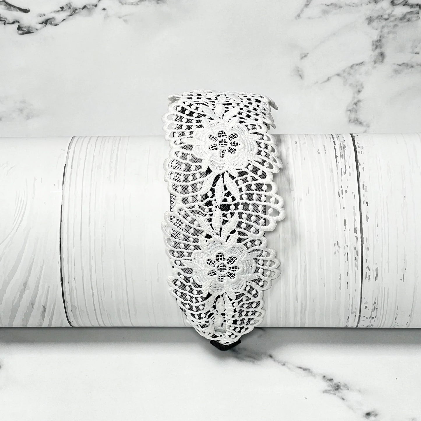 White floral broad lace hairbands with intricate pattern displayed on white textured surface