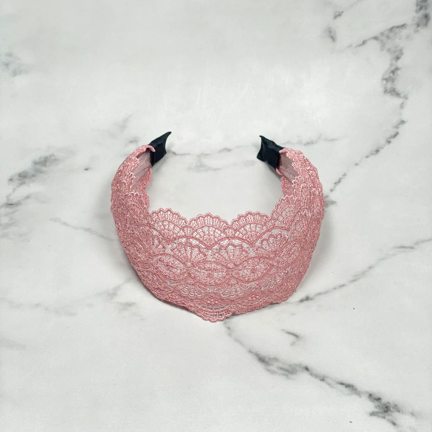 Pink broad lacy hairband with intricate floral lace pattern on a marble surface