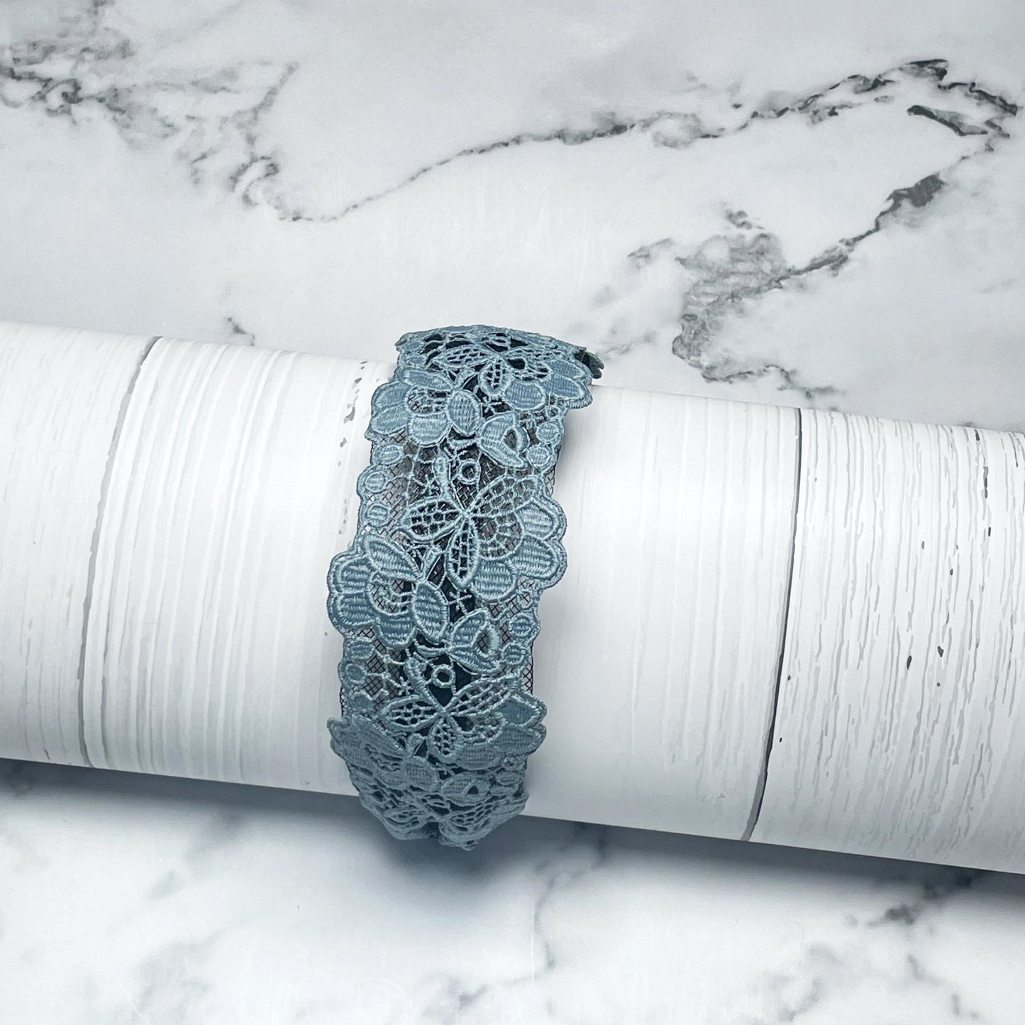 Blue broad lacy hairbands with floral design displayed on white textured surface