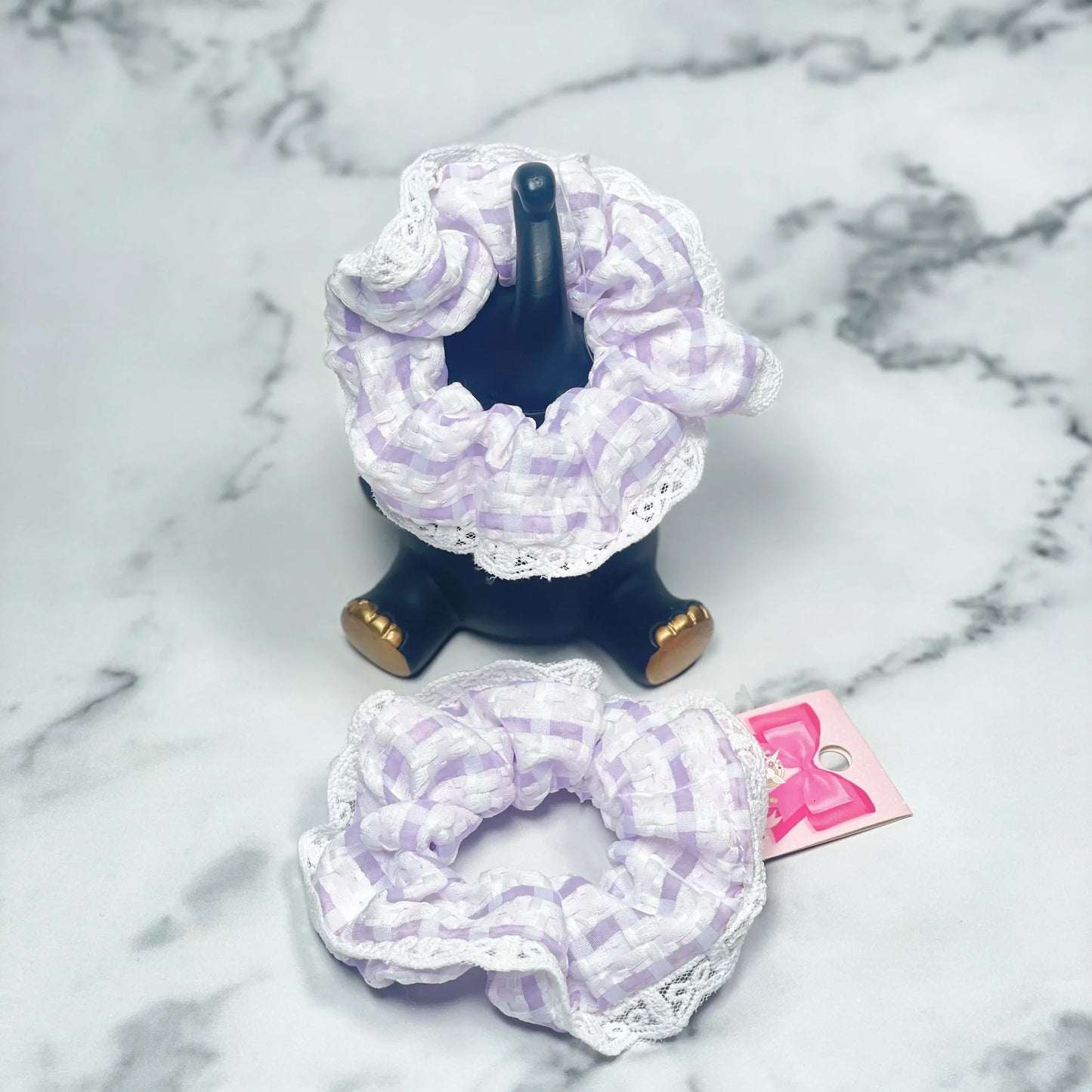 Purple check scrunchies with lace displayed on black holder and marble surface