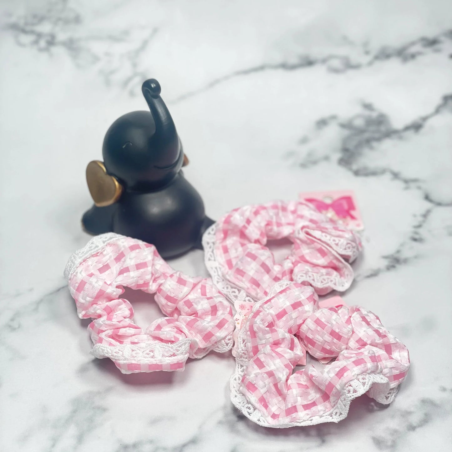 Pink and white check scrunchies with lace trim displayed on marble surface