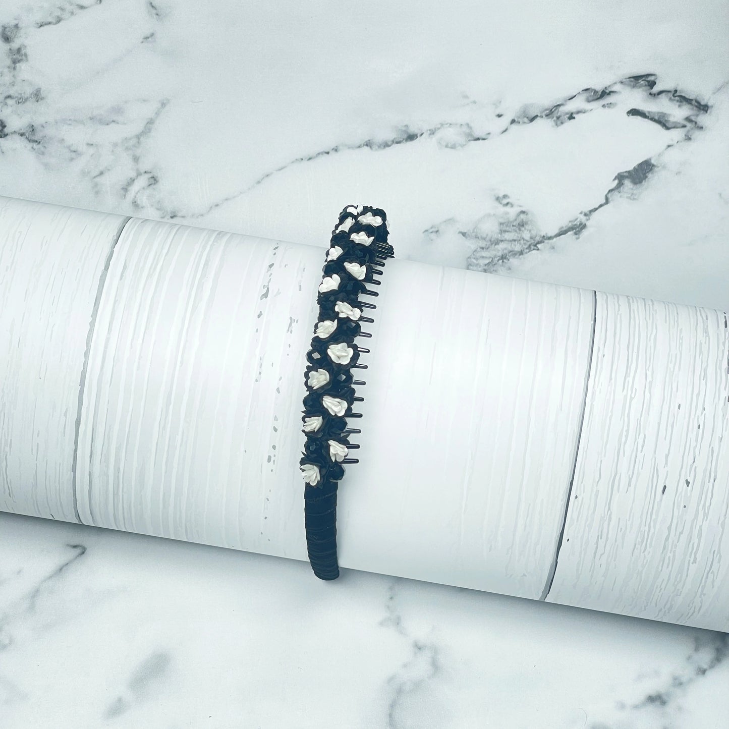 Black crystal flower studded hairbands with white floral accents on a white textured surface