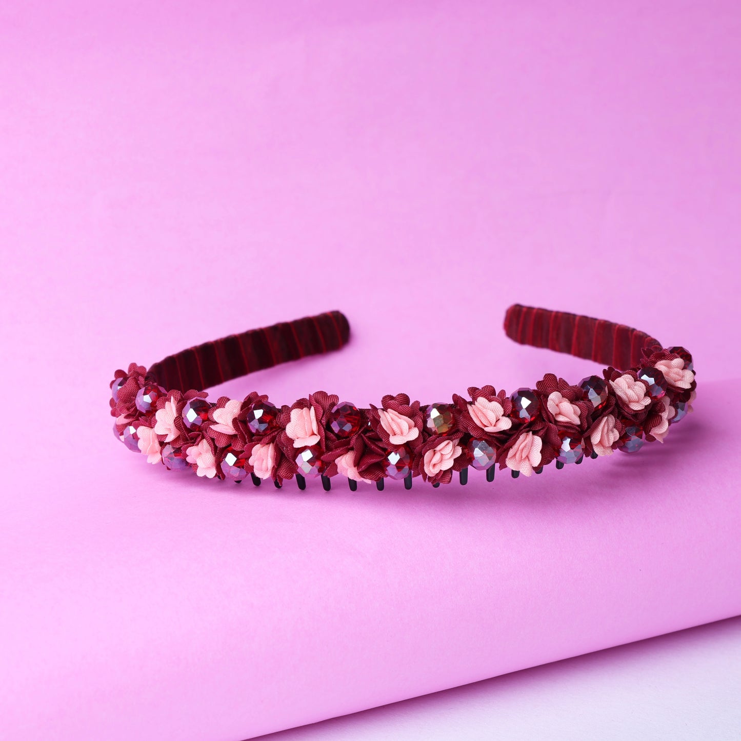 Red crystal flower studded hairbands adorned with pink and maroon floral decorations on a pink background