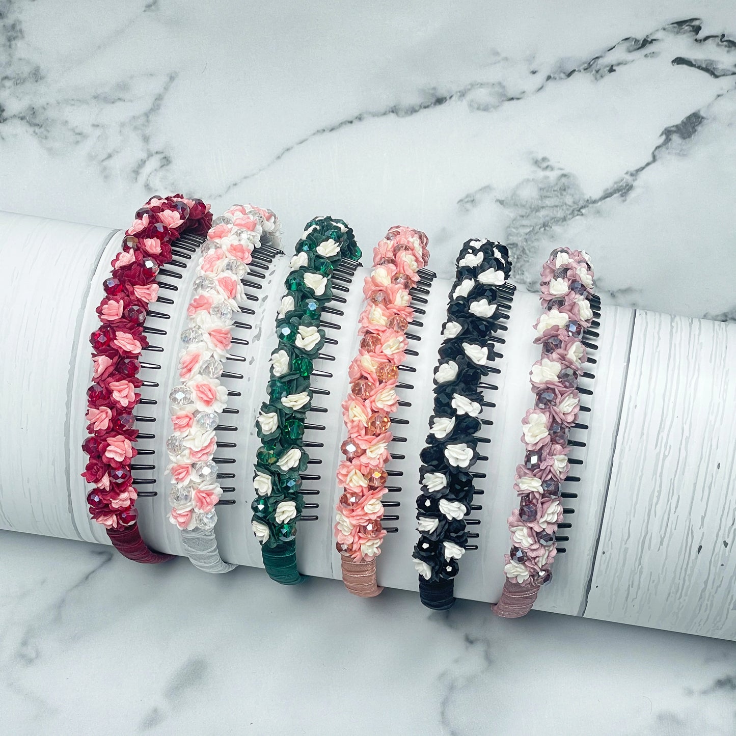 Set of six colorful crystal flower studded hairbands with small blooming flowers on a marble background