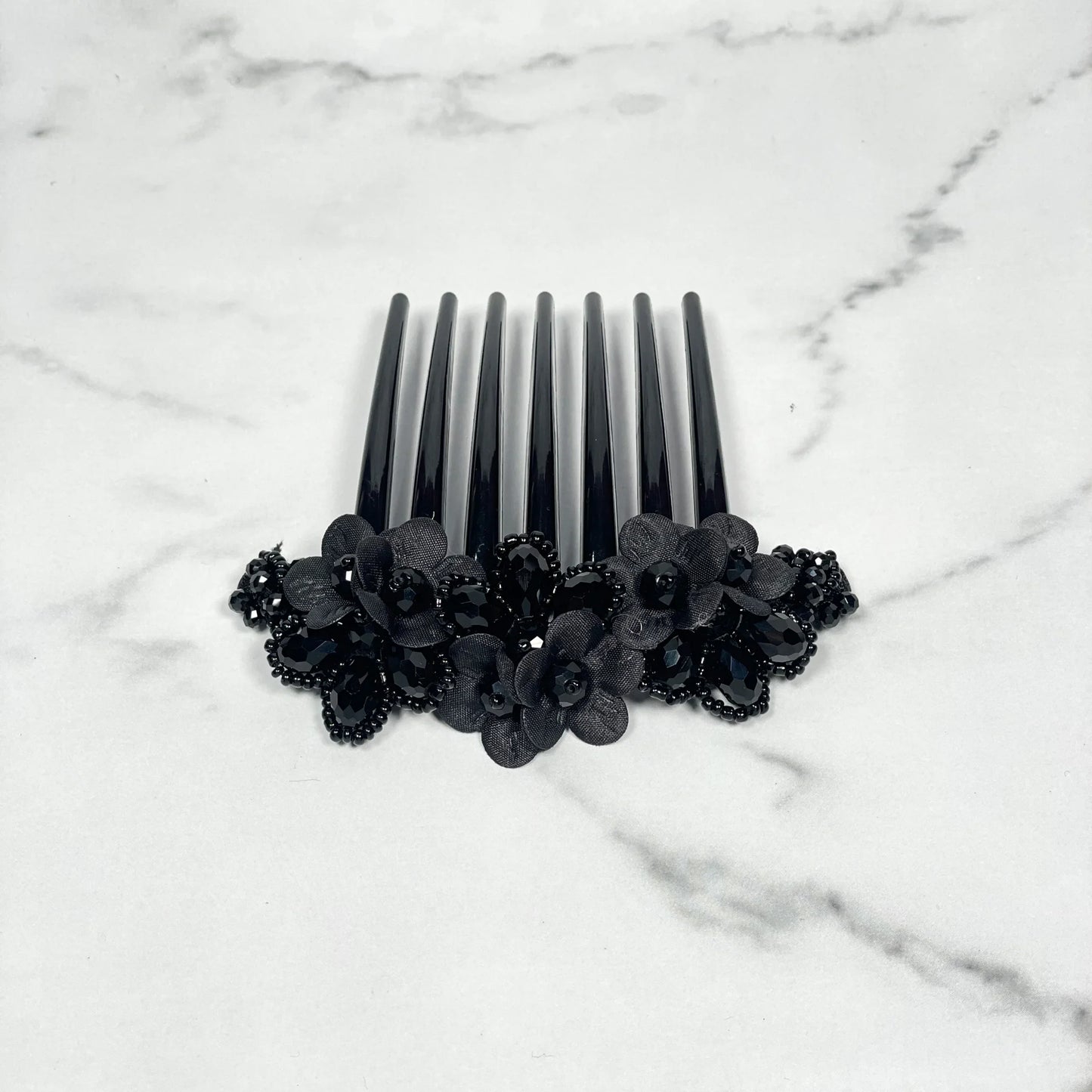 Black crystal studded comb clips with floral design on a white marble surface