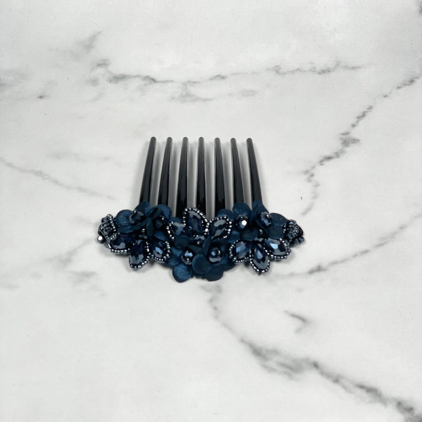 Black hair comb with crystal studded comb clips featuring decorative dark blue flowers on marble background
