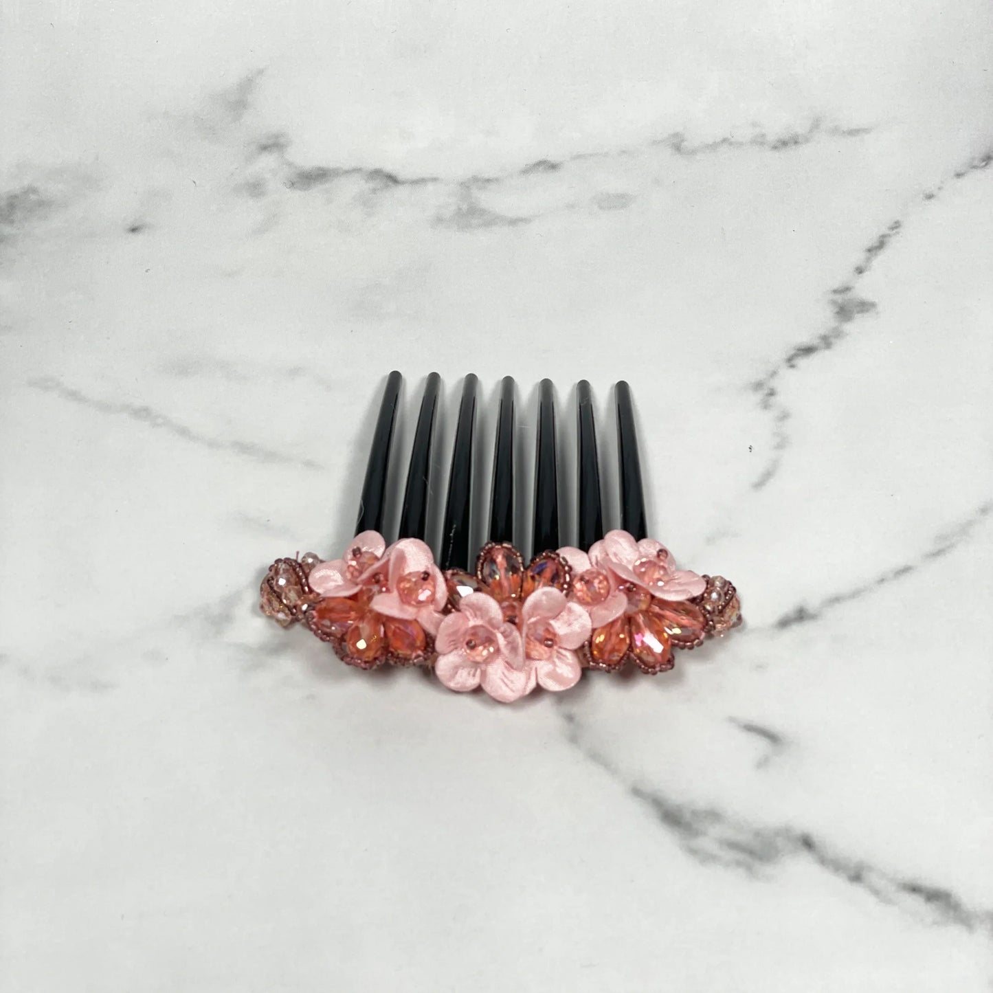Black hair comb with pink flowers and crystal studded comb clips embellishments on marble surface