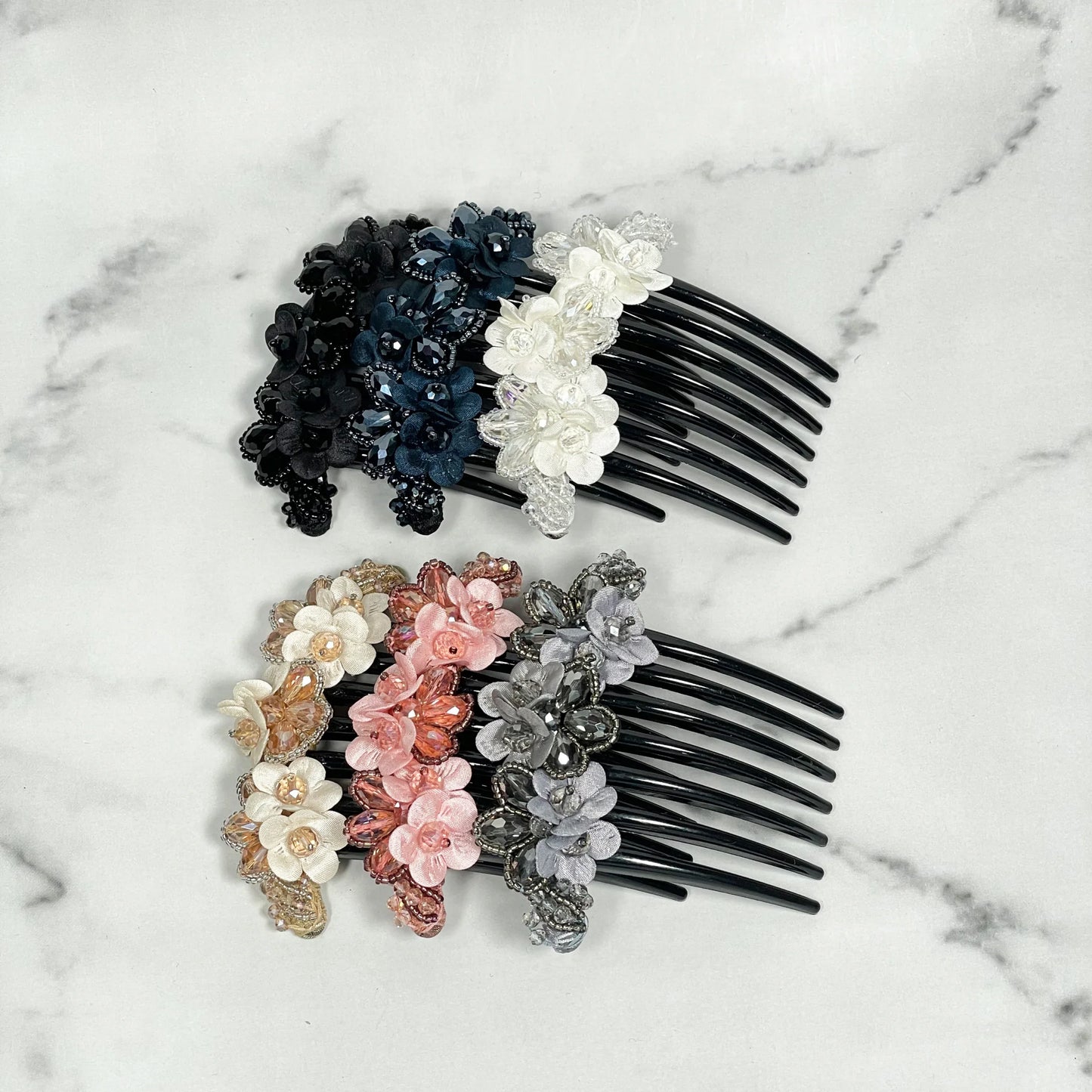 Set of flower design crystal studded comb clips in black, white, pink, gold, and silver colors on marble background
