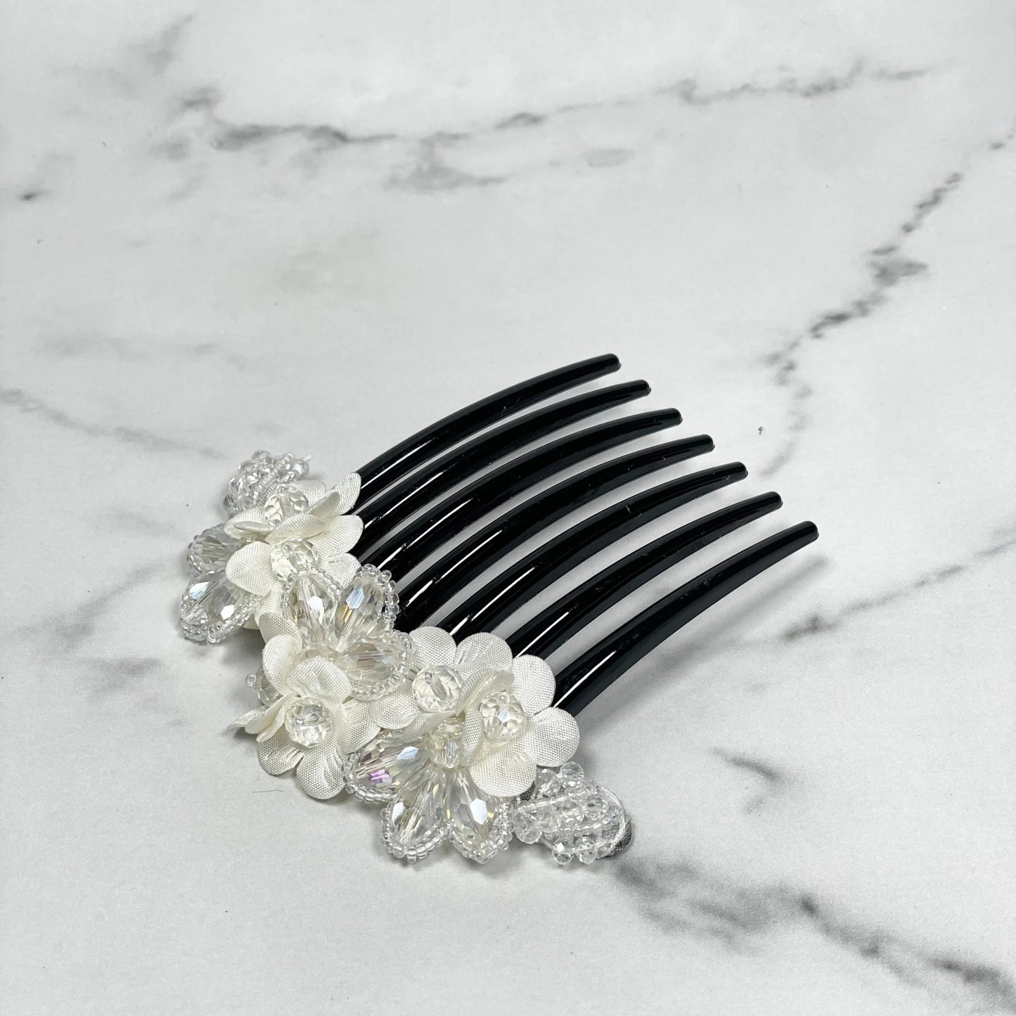 Black comb with crystal studded comb clips featuring white flowers and clear crystals on marble background