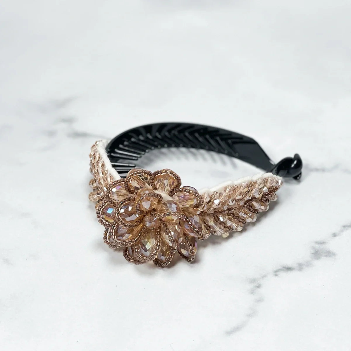 Elegant crystal studded hair bun clip with a floral design and beige decorative accents on black comb base