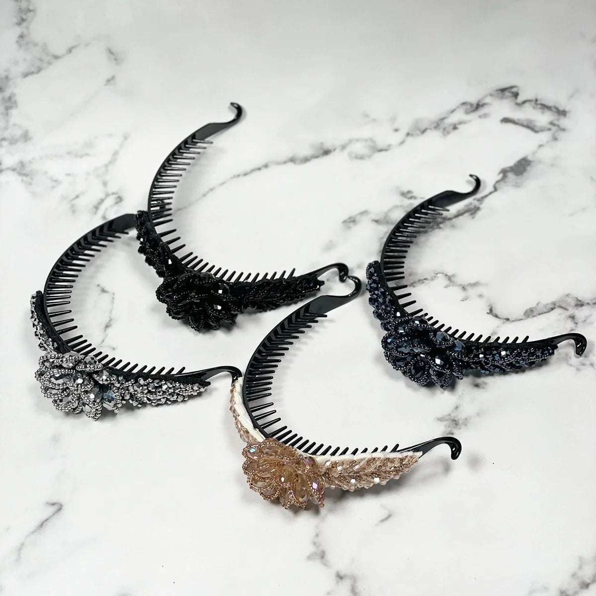 Set of four crystal studded hair bun clips in black, silver, and gold colors on marble background