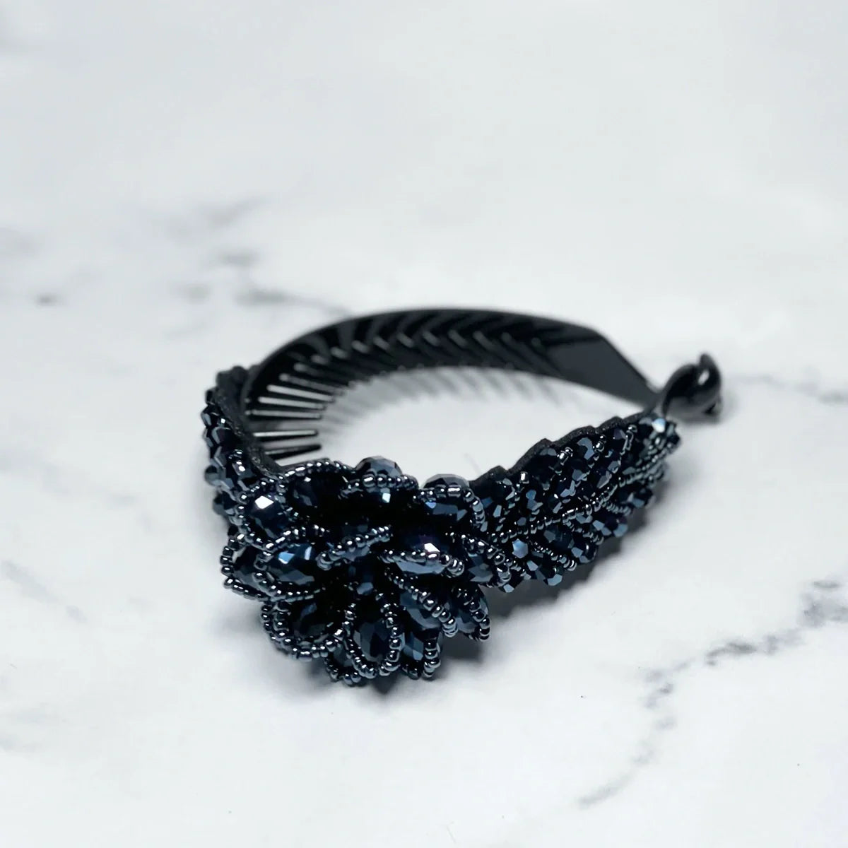 Black crystal studded hair bun clip with floral design on marble surface