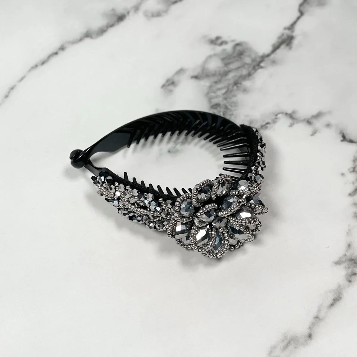 Black plastic crystal studded hair bun clip with intricate floral design on a marble surface