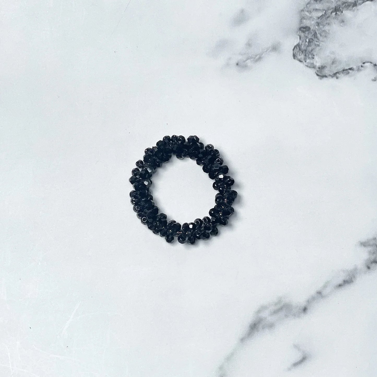 Black crystal studded hair ties with glossy beads on white marble background