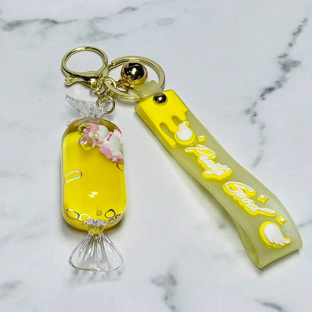 Yellow fancy key chain with candy-shaped charm and drip design on white marble background