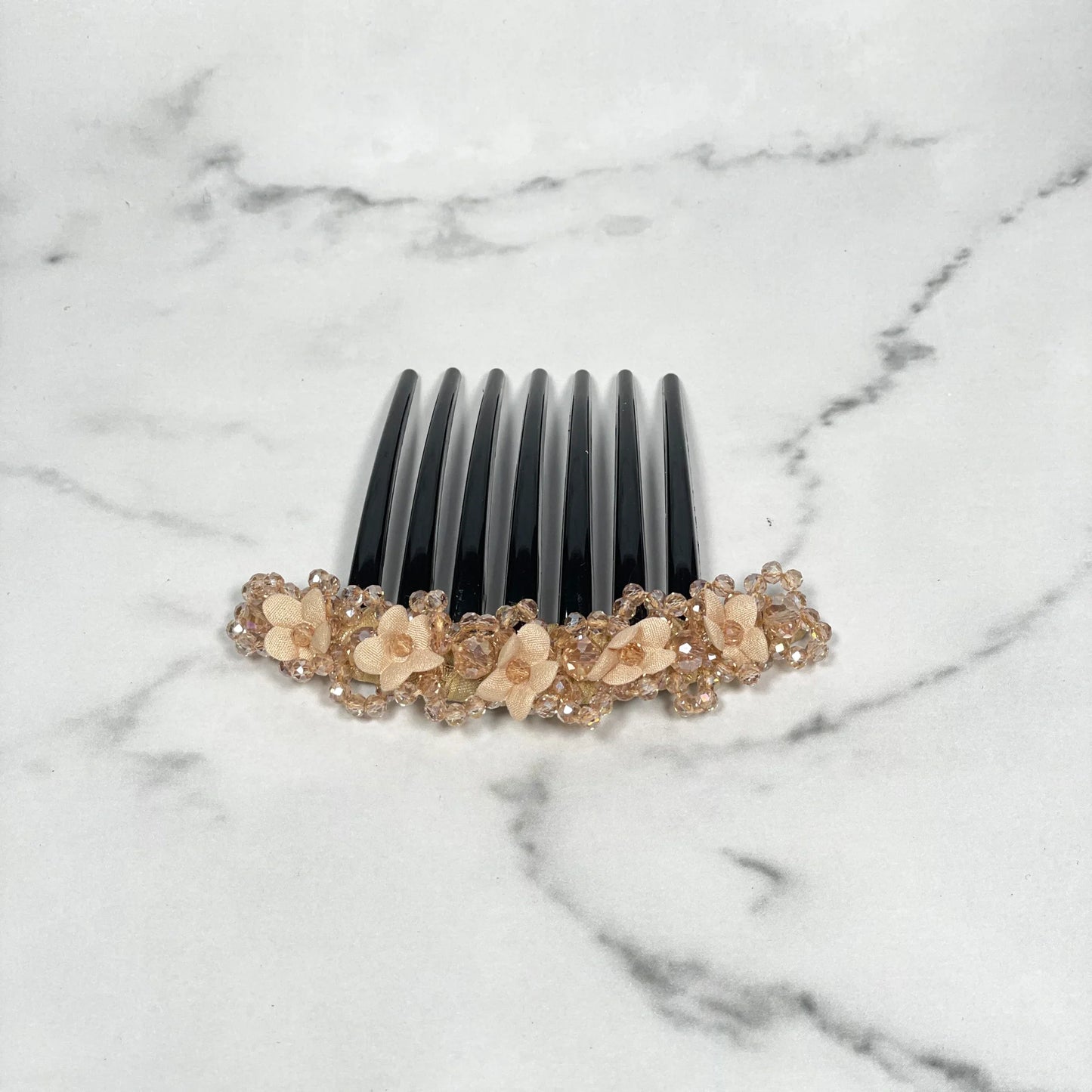 Black comb hair clip decorated with beige floral beaded hair comb clips on white marble background