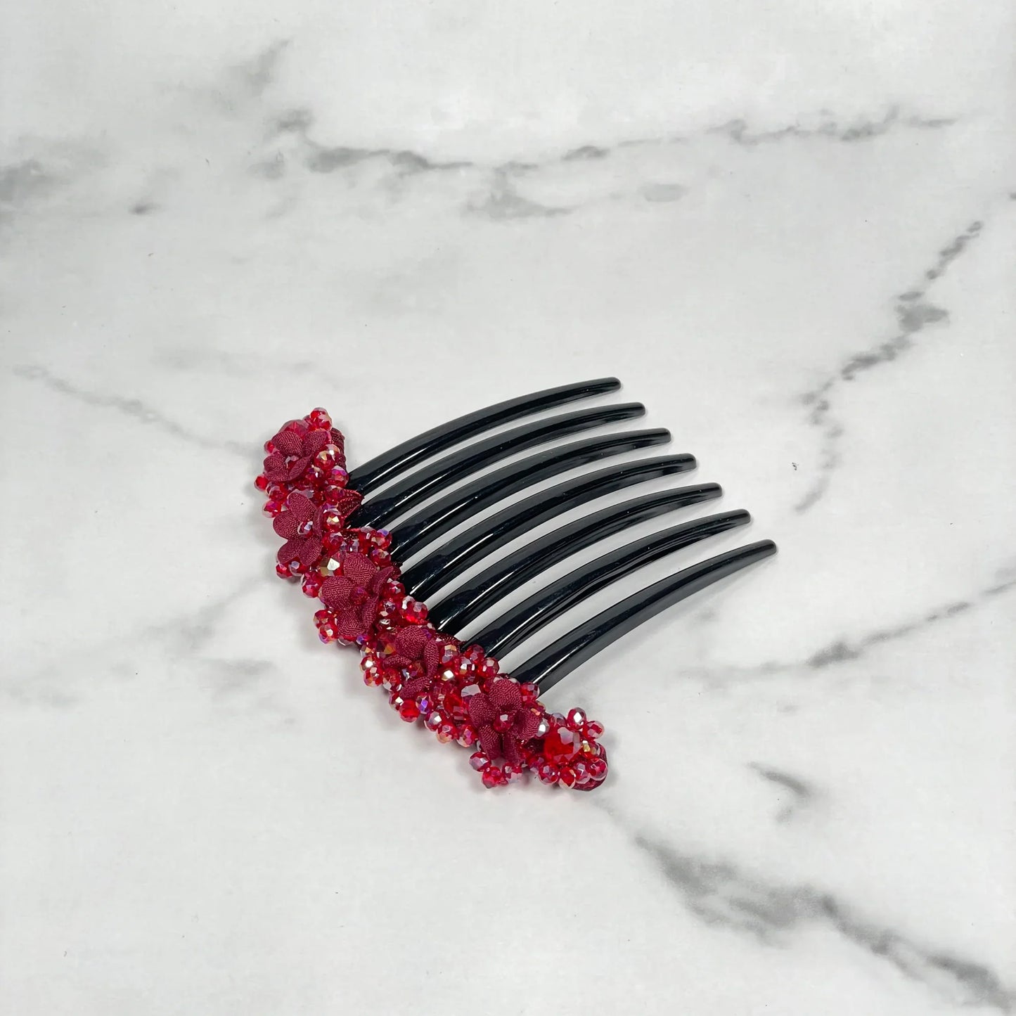 Black hair comb decorated with red floral beaded hair comb clips on white marble surface