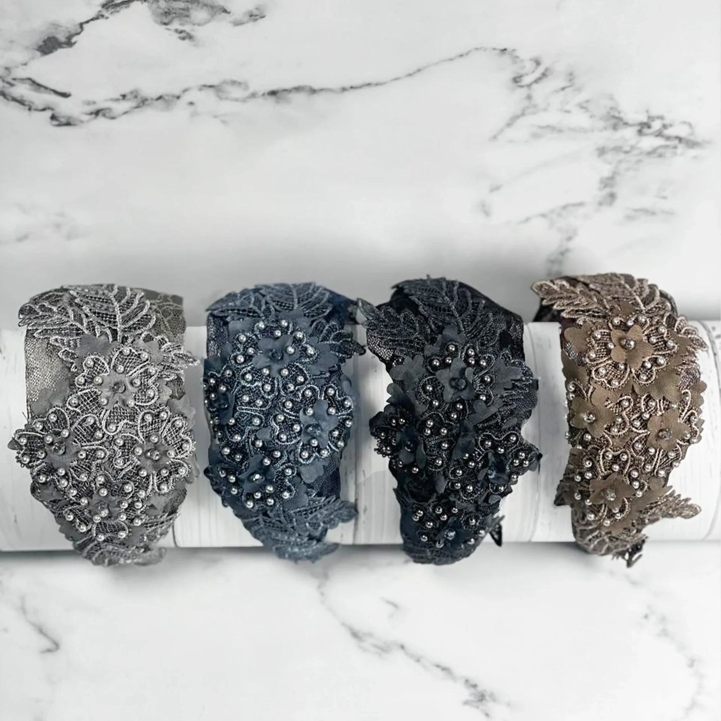 Four floral lacy hairbands with cutwork in gray, blue, black, and taupe colors displayed on a white marble surface