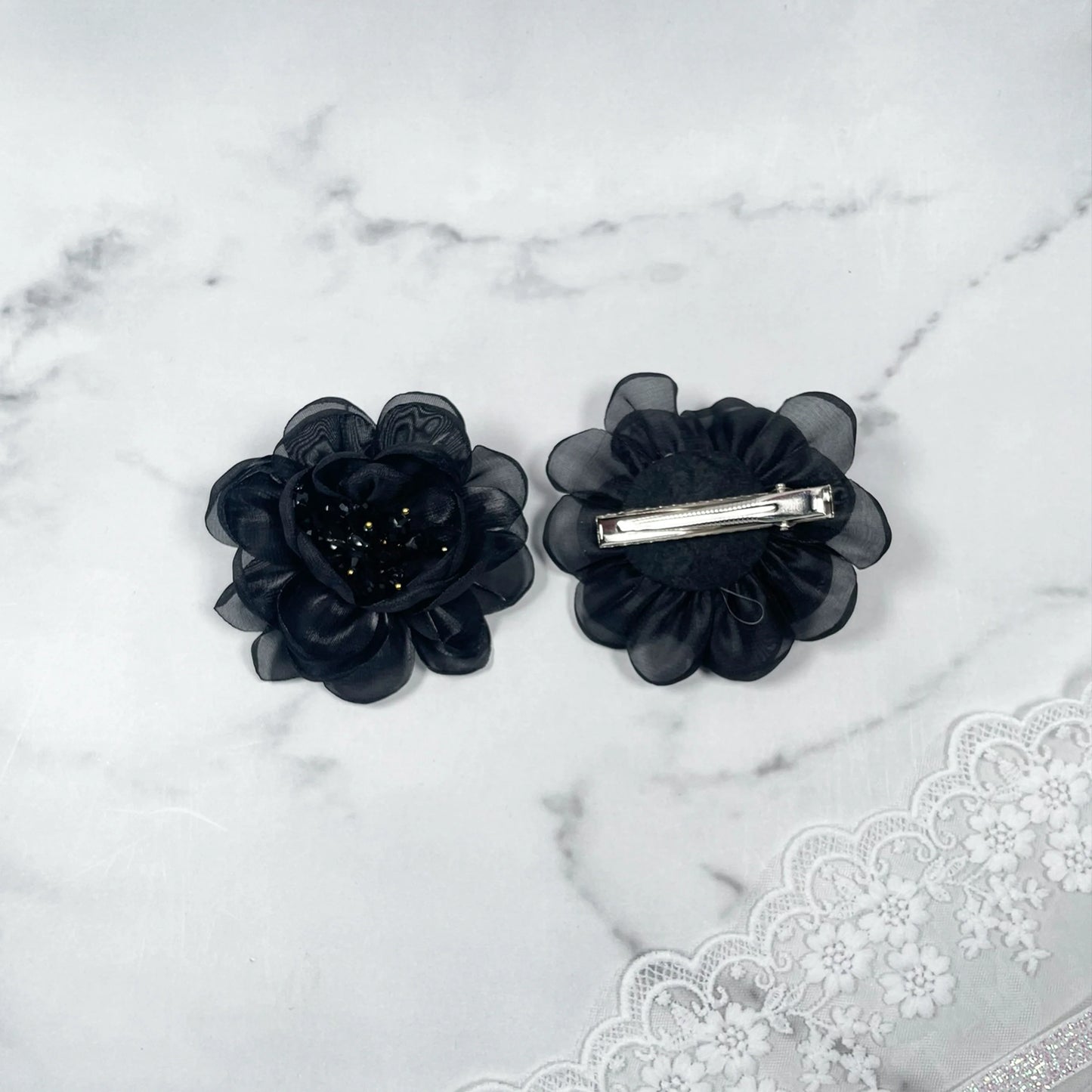 Black floral organza hair pins with layered petals and silver clips on a marble surface