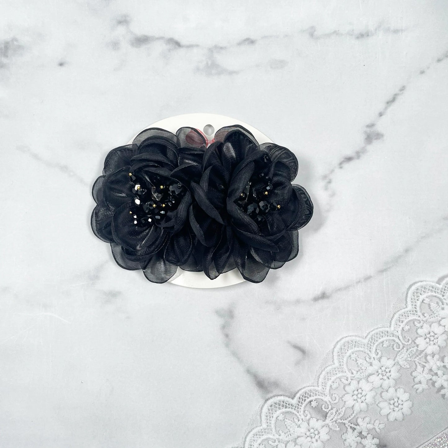 Black floral organza hair pins with beaded centers on white card with lace background