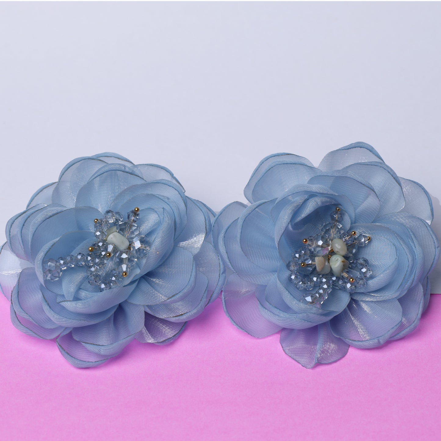 Two blue floral organza hair pins with bead and crystal centers on a pink and white background