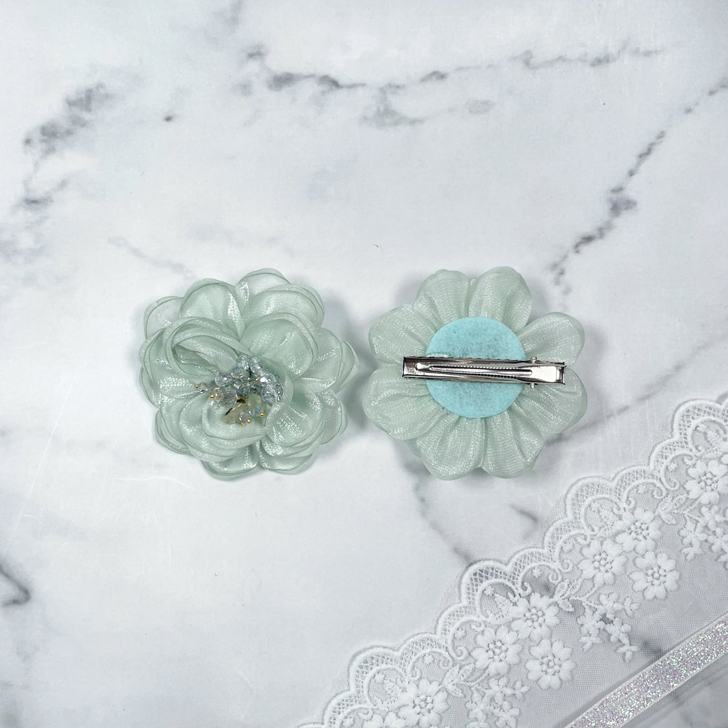 Light green floral organza hair pins with delicate bead embellishments on a marble surface