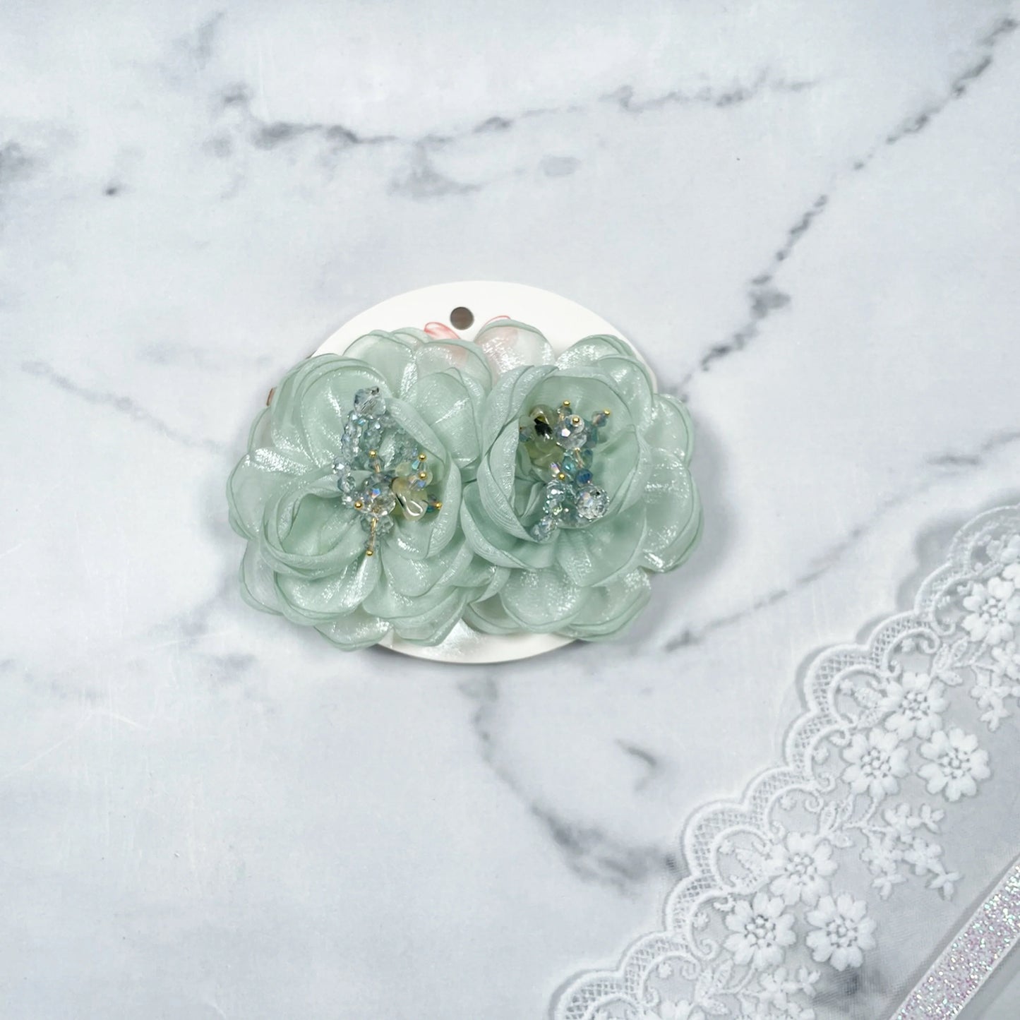 Mint green floral organza hair pins with bead embellishments on white card with lace background