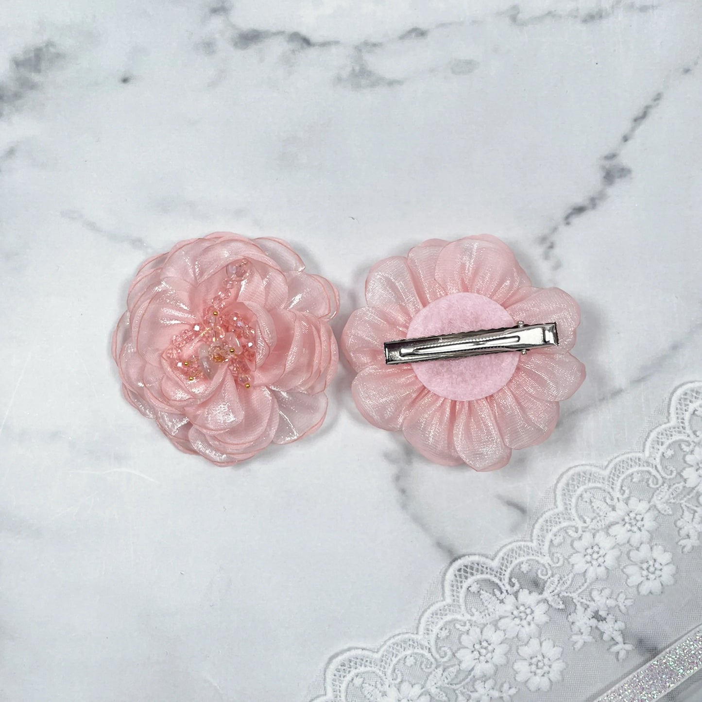 Pink floral organza hair pins with delicate translucent petals and metal clip on marble background