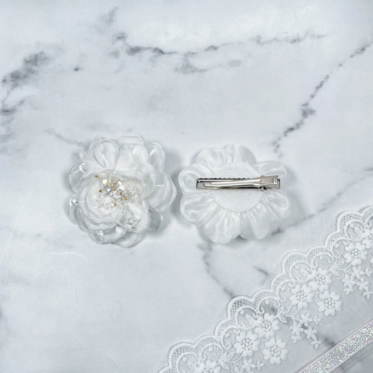 White floral organza hair pins with pearl accents displayed on marble background with lace trim