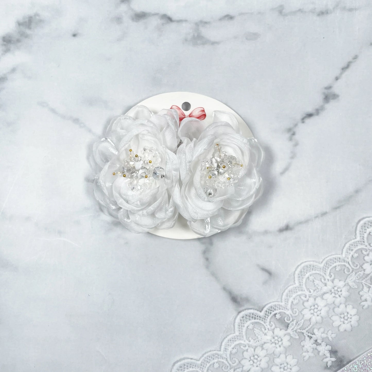 White floral organza hair pins with pearl and bead accents displayed on round white card