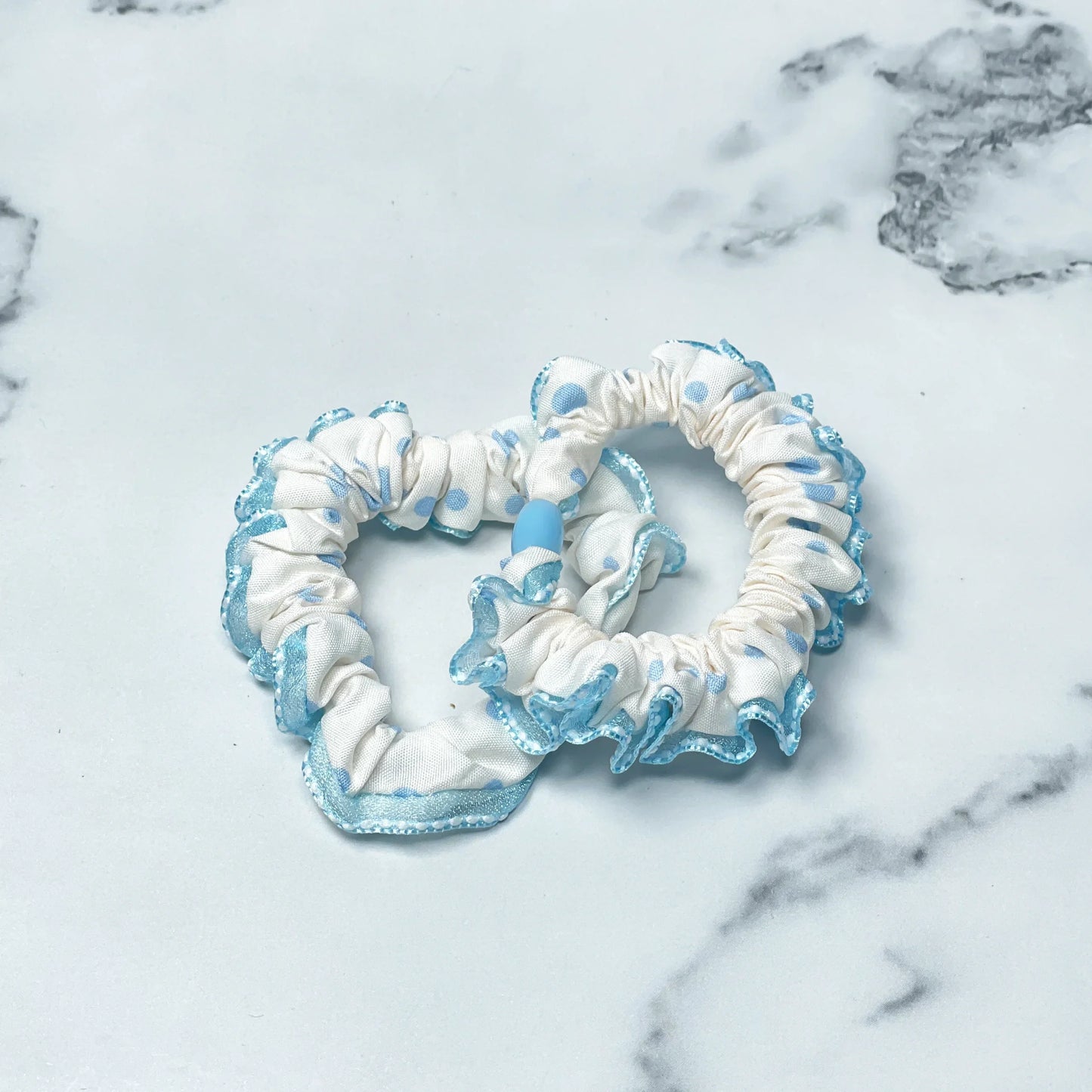 White and blue frill polka dot hair ties with ruffled edges on marble background