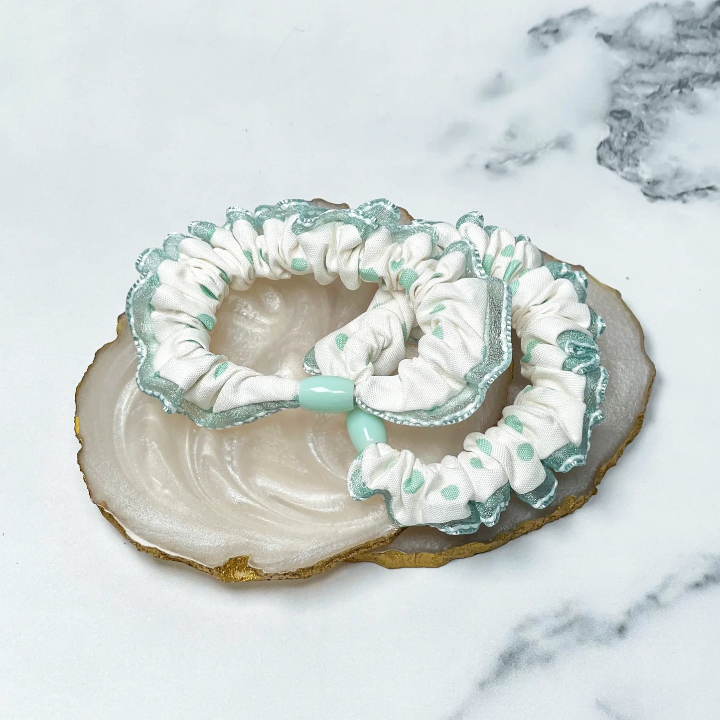 White and mint green frill polka dot hair ties with scalloped edges on a marble surface