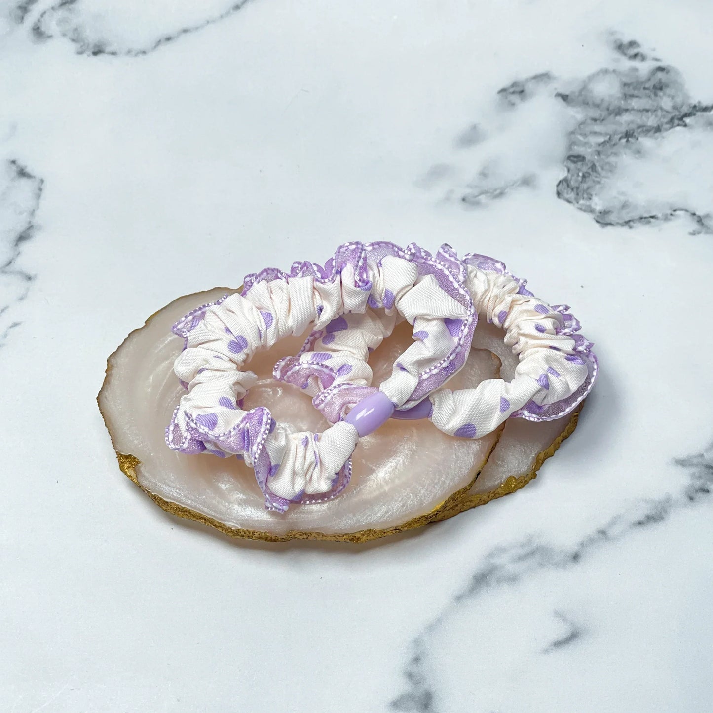 Frill polka dot hair ties in white and lavender with delicate edges displayed on a marble surface