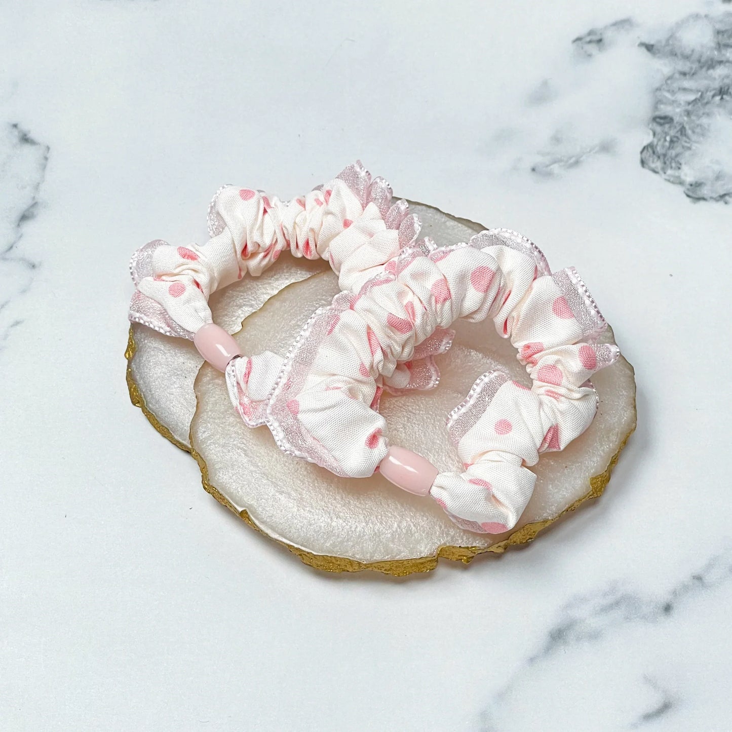 Frill polka dot hair ties in white and pink with ruffled edges displayed on a marble background
