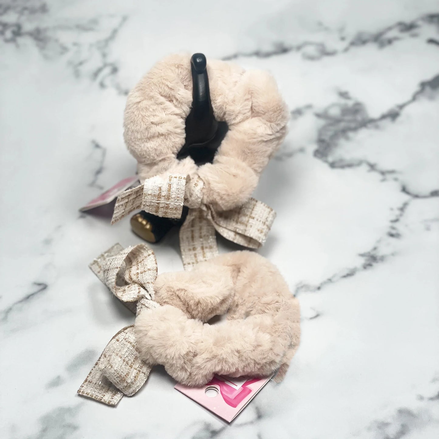 Beige fur scrunchie with check ribbon tied in bow, displayed on marble surface