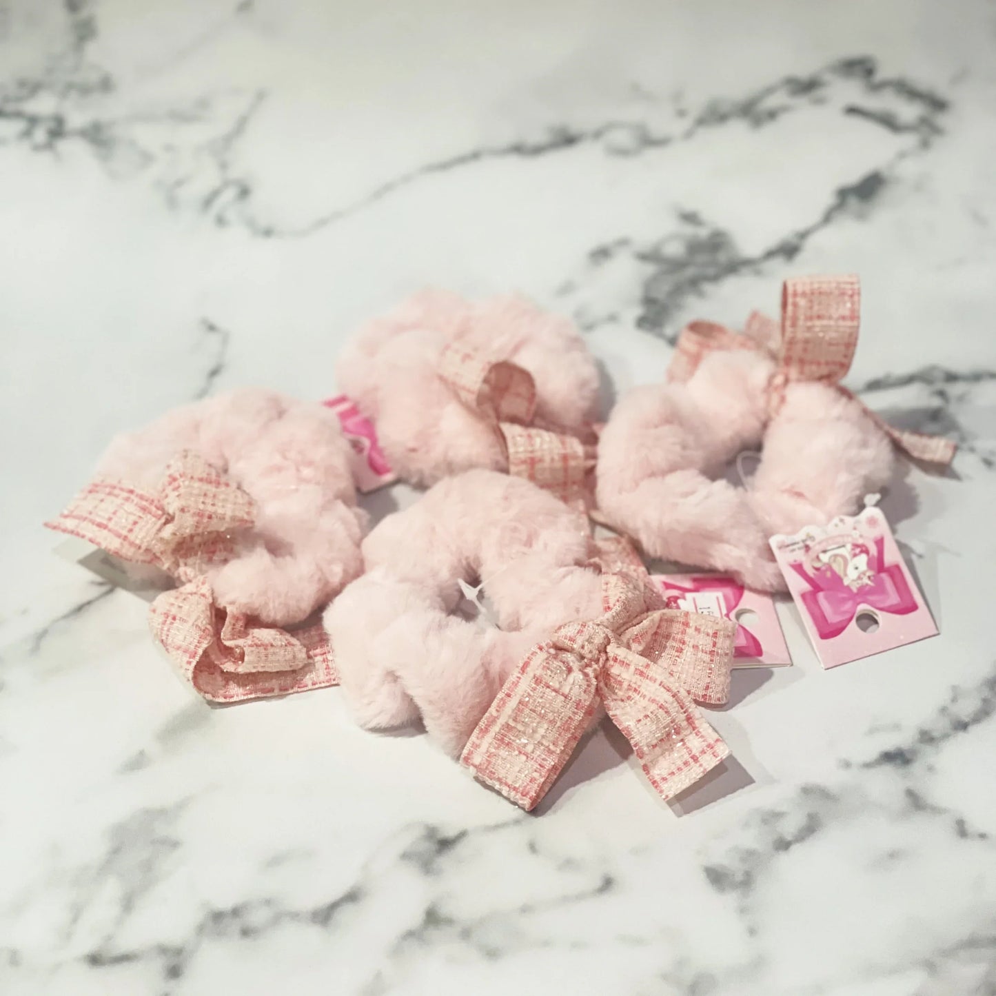 Pink fur scrunchie with check ribbon displayed on marble surface from mydevelopmentstor
