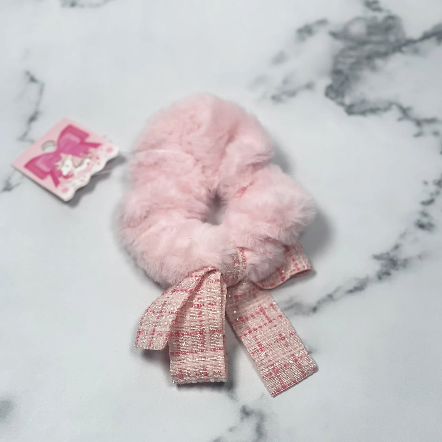 Soft pink fur scrunchie with check ribbon tied in a bow on marble surface fur scrunchie with check ribbon