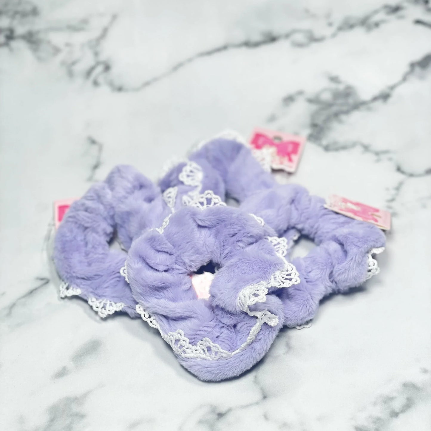 Purple fur scrunchies with lace edges arranged on a marble surface by mydevelopmentstor