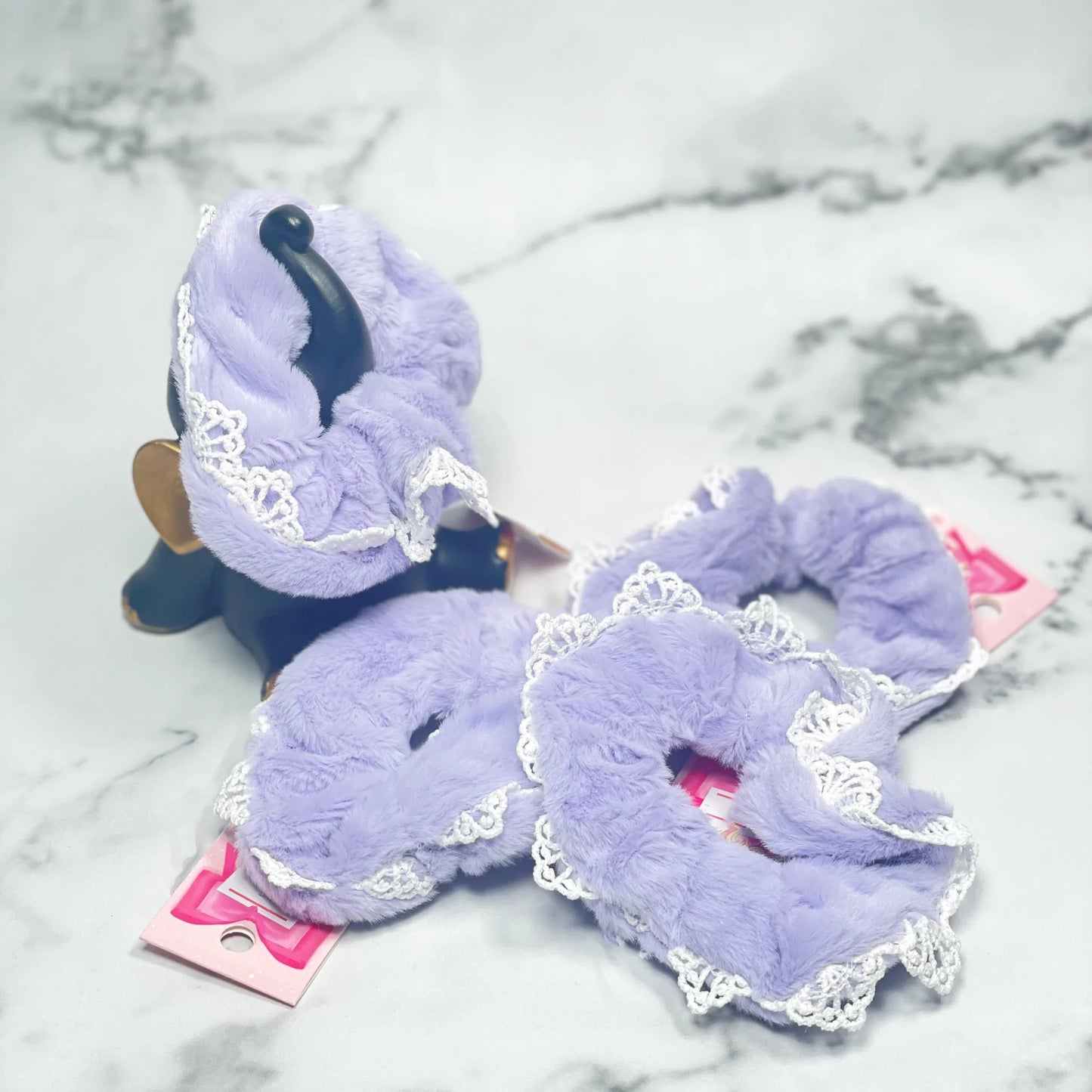 Lavender fur scrunchies with lace trim displayed on a marble surface for stylish hair accessories