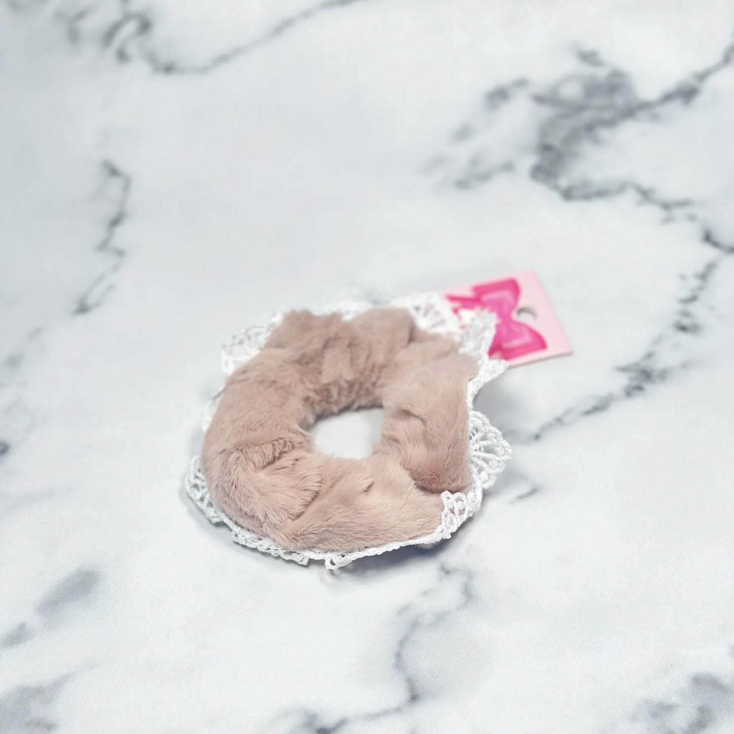 Beige fur scrunchies with lace trim displayed on marble surface for stylish hair accessories
