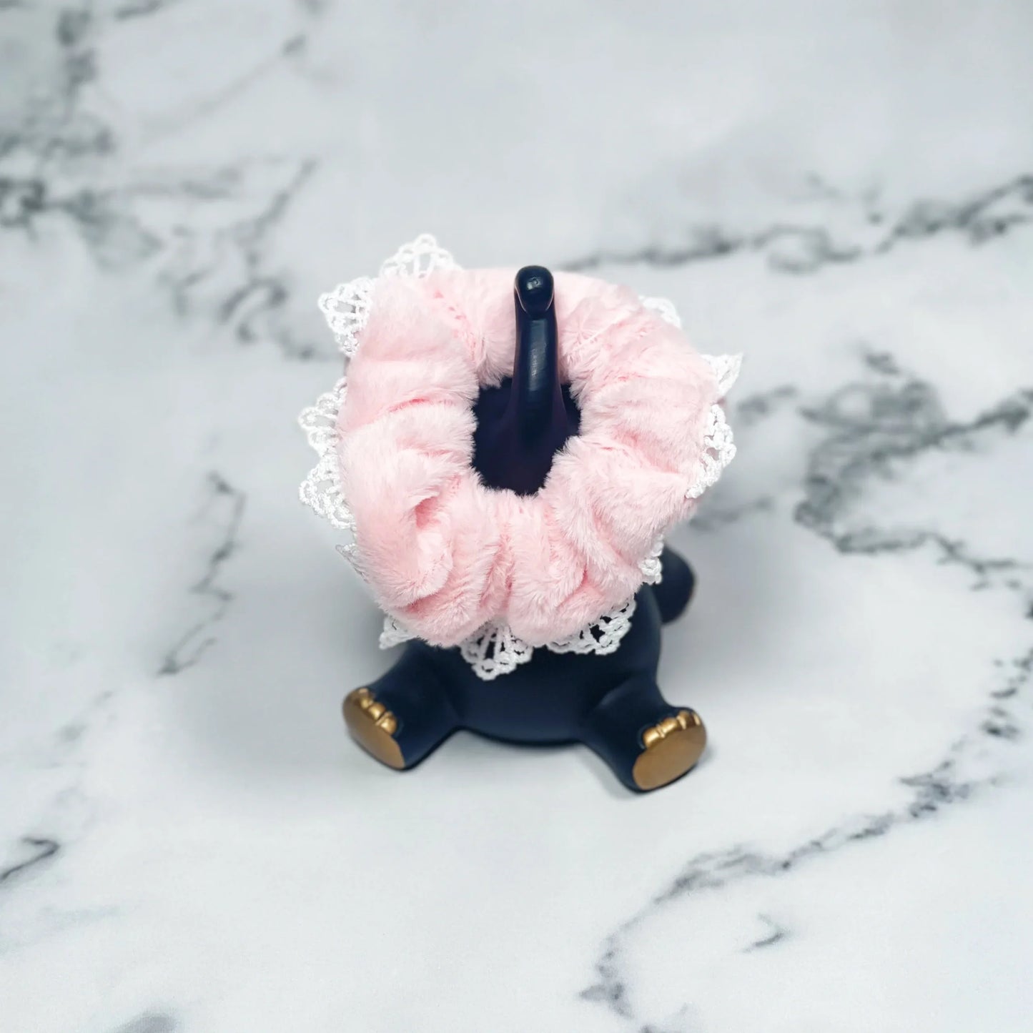 Pink fur scrunchies with lace displayed on a black hand-shaped holder on marble surface